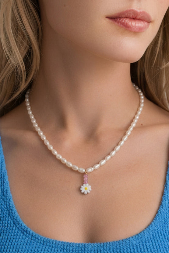 A close-up of a woman wearing a delicate pearl necklace with a small pastel flower pendant, paired with a bright blue knit crop top.