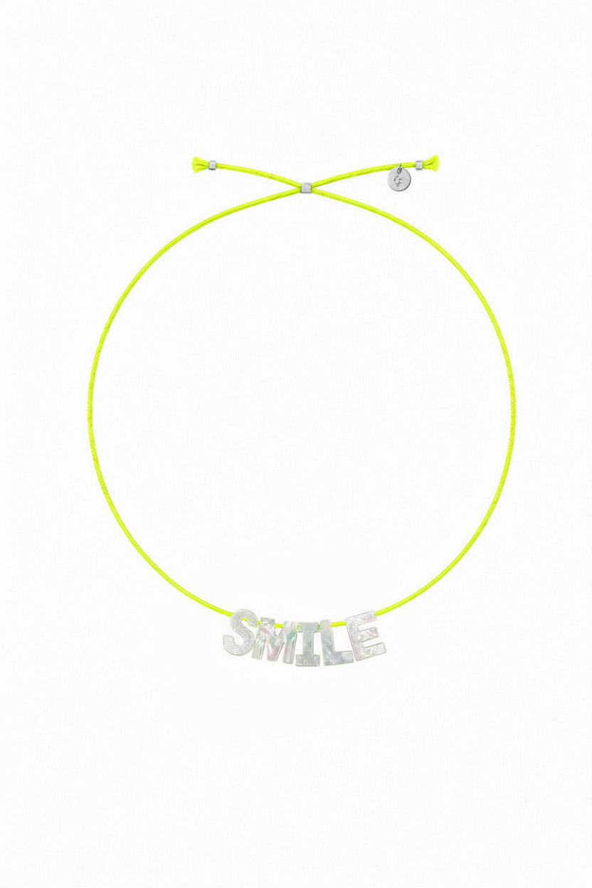 A neon green adjustable cord necklace with a silver-tone 'SMILE' charm spelling out the word, displayed on a clean white background.
