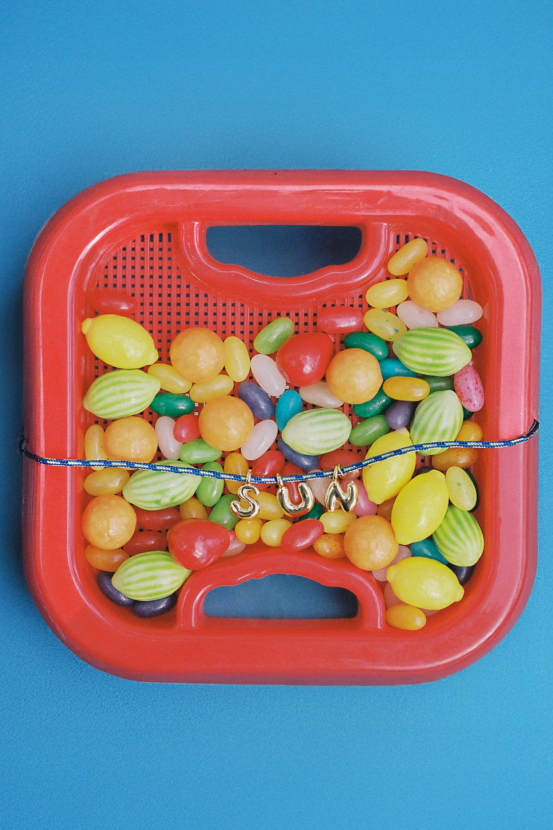 A red plastic candy basket filled with assorted colorful candies, tied with a blue string across the middle, set against a solid blue background.