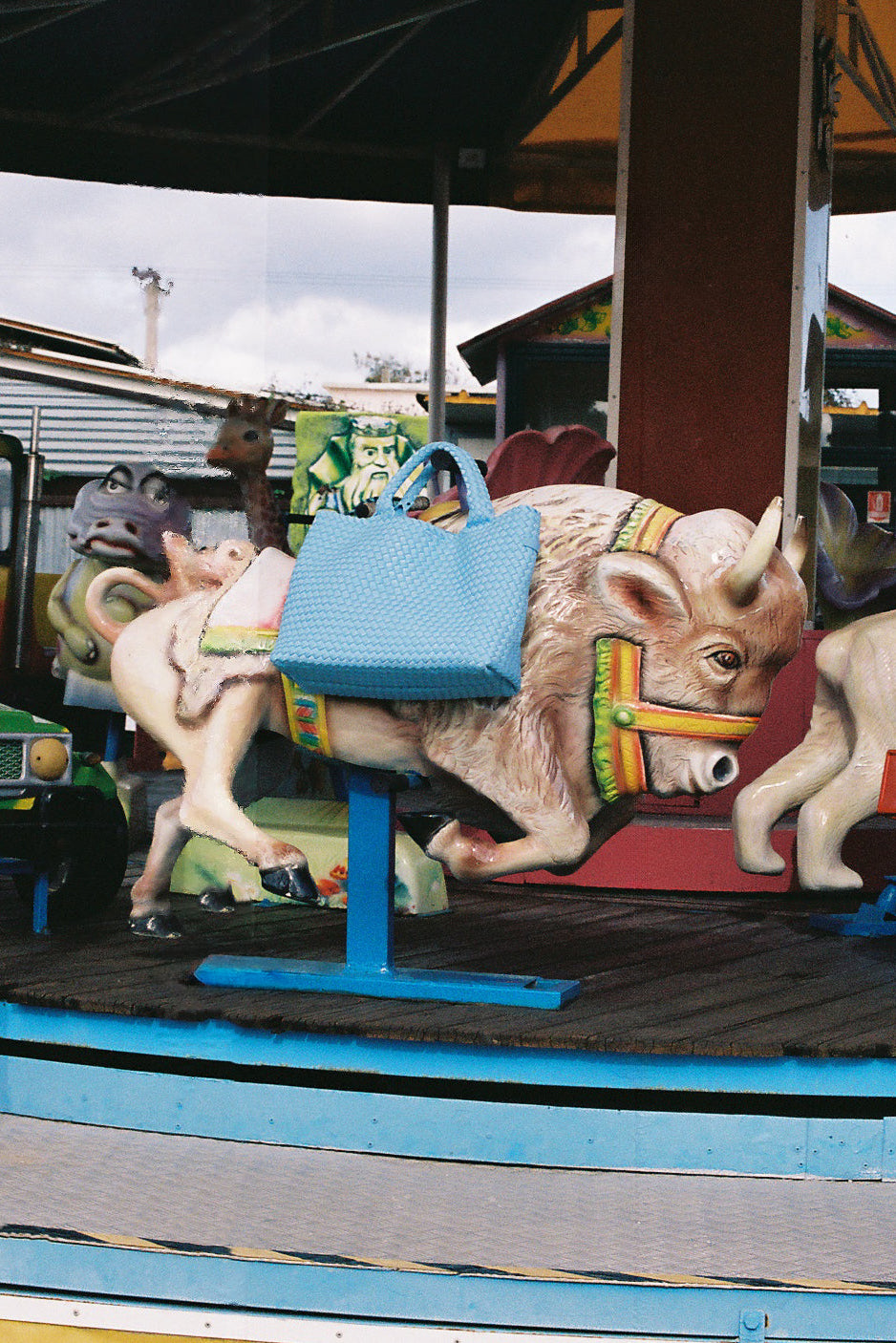 A vintage carousel ride with painted animal figures, including a central cow with a blue saddle and a white horse beside it, photographed outdoors under a canopy.