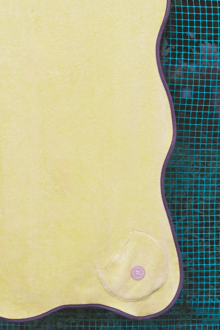 A close-up of a yellow fabric or leather-like curved panel with a small pink button detail, set against a teal grid-patterned background.